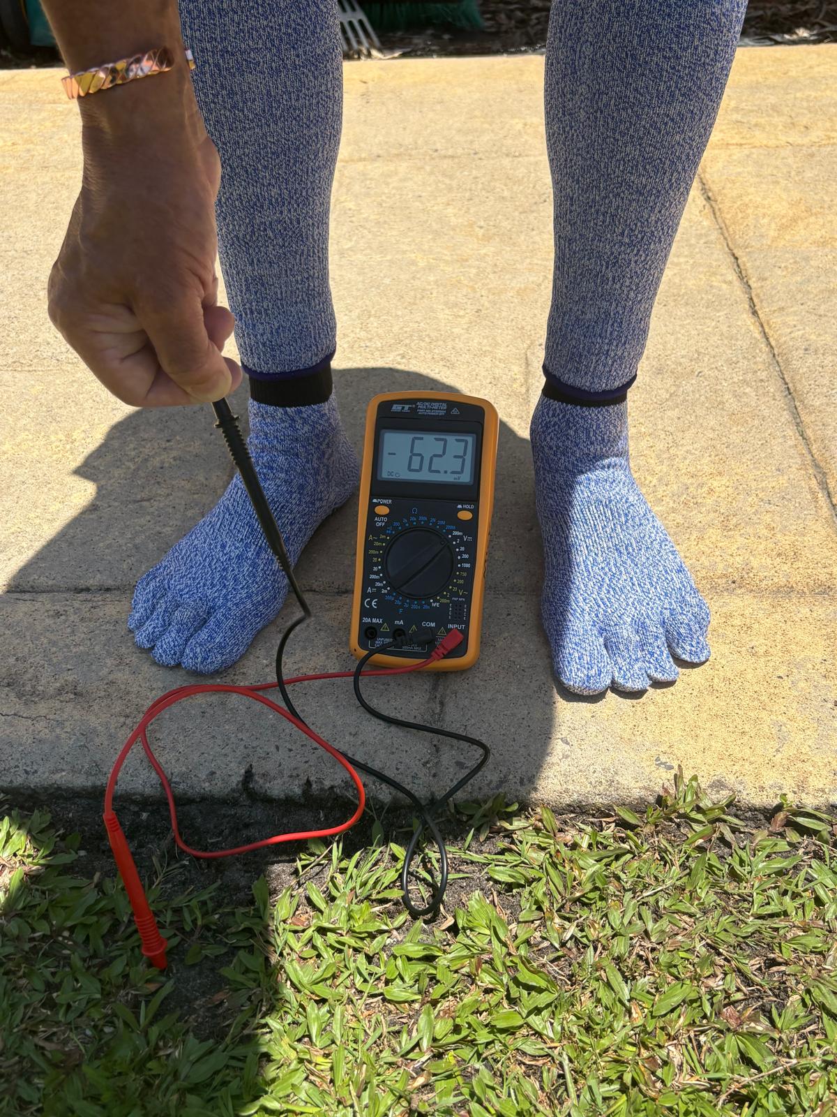 Person wearing toe-separated socks with a multimeter on a concrete surface.