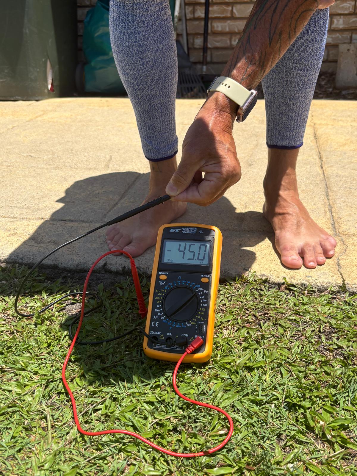 Person using a multimeter on grass with a digital display showing 45.0