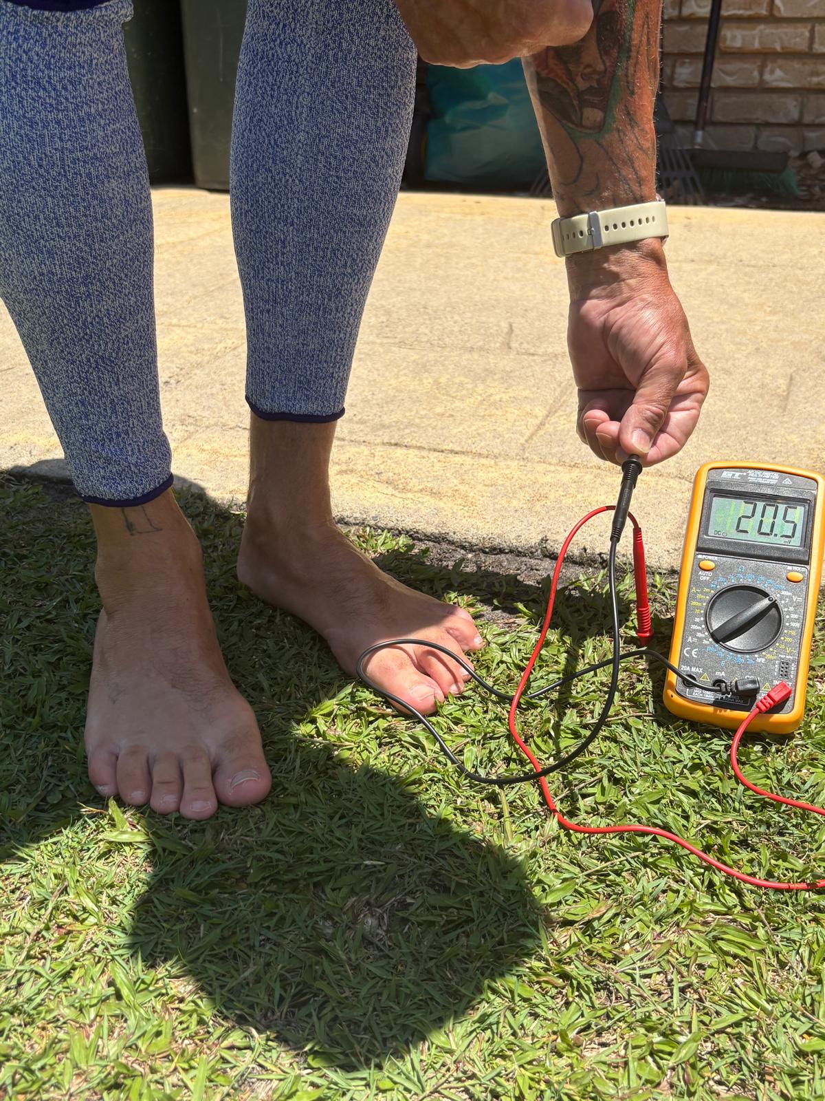 Person using a multimeter on grass with a brick wall in the background