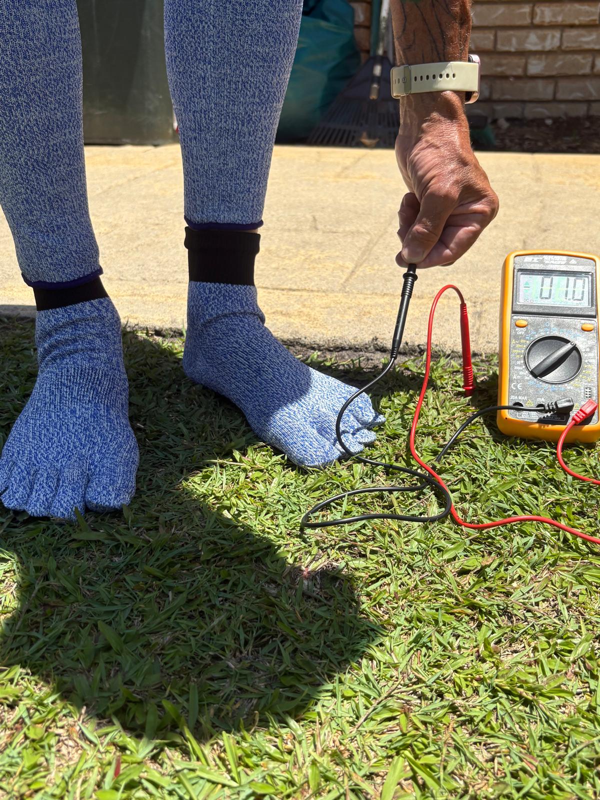 Person wearing blue socks with a multimeter on grass