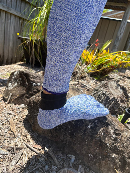 Person wearing blue textured socks on a rocky surface with plants in the background