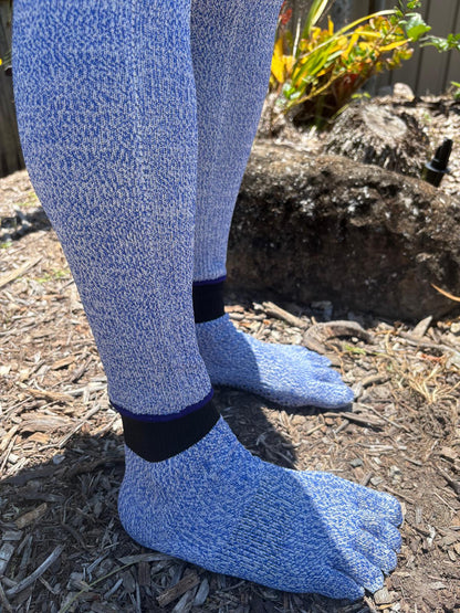 Blue fuzzy socks worn outdoors on a mulched surface with plants in the background