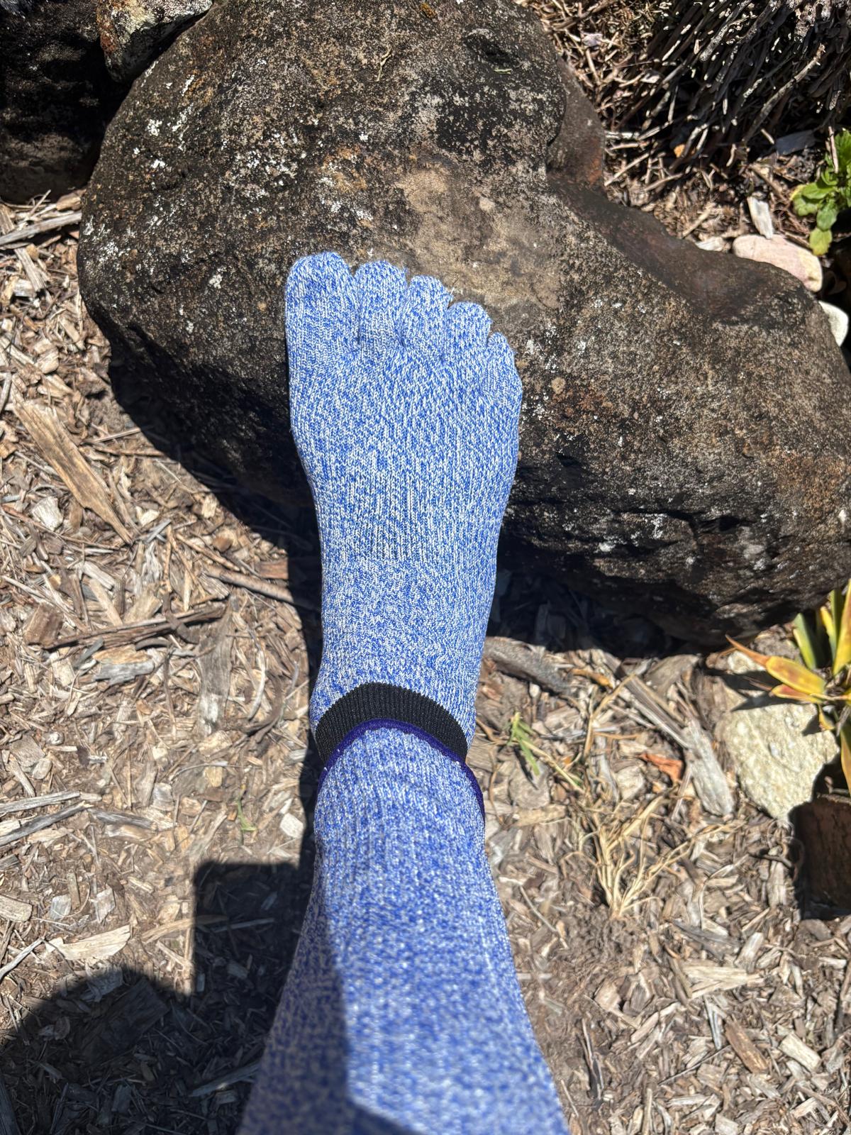 Blue sock on a foot against a natural background with rocks and dry leaves.